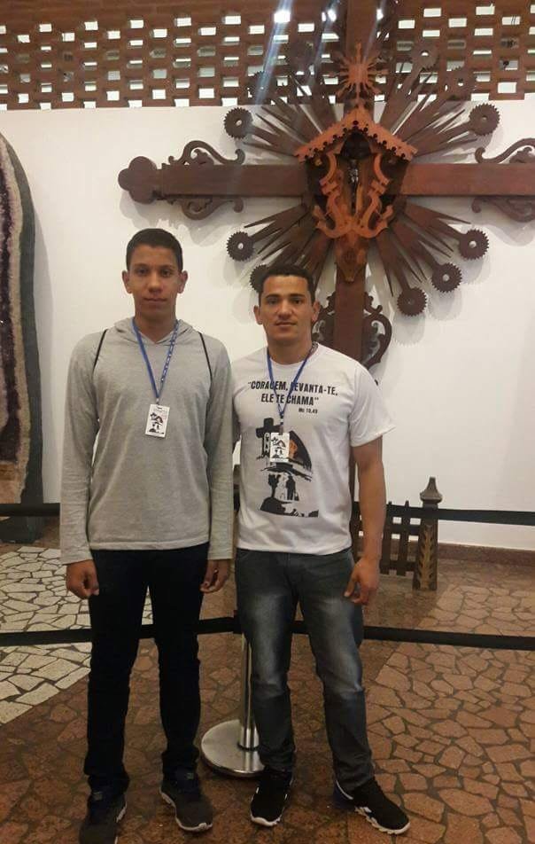 Dois participantes diante de uma cruz artesanal dentro do santuário
